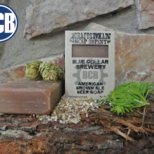 Op de afbeelding: Een bruine zeep met de tekst "Blue Collar Brewery BCB American Brown Ale Beer Soap" op een bruin kartonnen label. Het label heeft een tandwielontwerp en de tekst "Craftsman Soap Company".