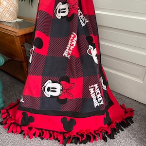 May include: Red and black fleece blanket with a checkered pattern and Mickey and Minnie Mouse images. The blanket has a knotted fringe border.