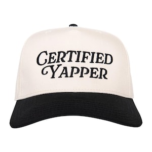 May include: A baseball cap with a cream-colored crown and a black brim. The phrase "CERTIFIED YAPPER" is embroidered in black script across the front. The cap has a black button on top.