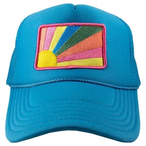 May include: A turquoise trucker hat with a colorful embroidered patch. The patch features a yellow sun with rainbow rays in pink, orange, green, and blue. The hat has a mesh back and a curved brim.