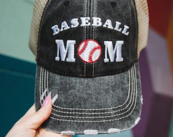 May include: Distressed black baseball cap with a tan mesh back. The front features the words "BASEBALL MOM" in white embroidery, with a baseball graphic in the center. The cap has a curved brim and a worn look.