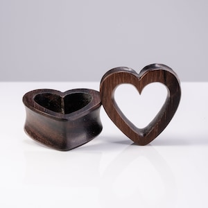May include: Two wooden heart-shaped ear gauges. One gauge is solid wood, the other has a heart-shaped cutout.