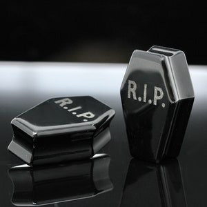 May include: Two black coffin-shaped ear gauges with the word "R.I.P." engraved on each.