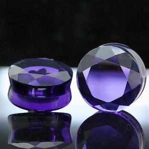 May include: Two purple glass ear gauges with a faceted design. The gauges are round and have a smooth, polished finish.