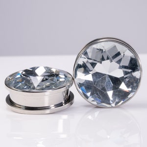 May include: Two silver ear gauges with clear faceted crystal plugs.