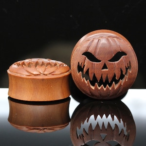 May include: Two wooden ear gauges, one with a carved floral design and the other with a carved jack-o'-lantern face.