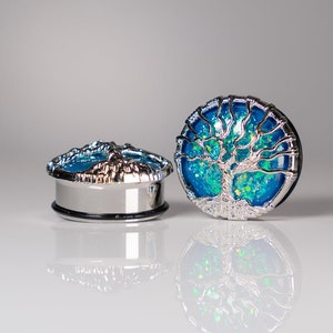 May include: A pair of silver ear gauges with a blue and green tree of life design. The gauges are made of metal and have a shiny finish.