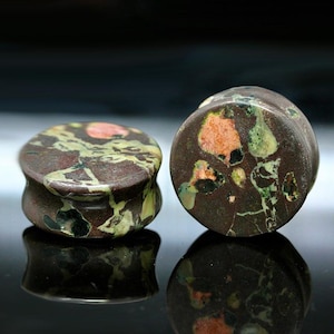 May include: A pair of circular ear plugs crafted from a dark brown stone featuring natural inclusions of mottled green, black, and salmon pink. The plugs have a smooth, polished finish with a concave profile, showing distinct mineral patterns.