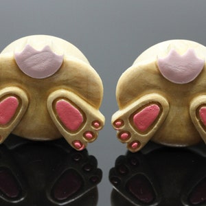 May include: A pair of wooden ear gauges with a bunny rabbit design. The gauges are painted brown with pink accents for the tail and feet.
