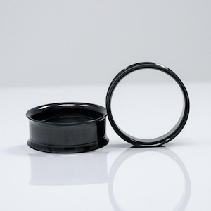 May include: Two black ear gauges, one is a flared style and the other is a simple ring style.