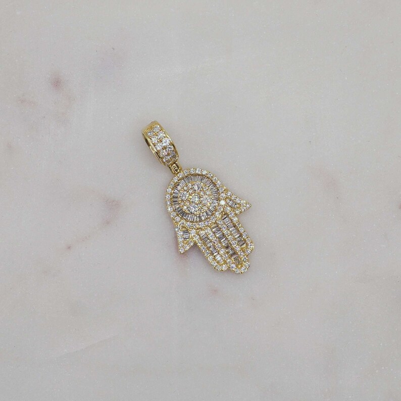 10k solid gold Hamsa hand charm pendant for protection, mini size fine jewelry. 10k gold Hamsa charm styled with beach-inspired gold jewelry on neutral background
