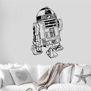 May include: Black and white silhouette of R2-D2, a fictional robot character from the Star Wars franchise, on a white wall. The robot is standing on a white couch with throw pillows.