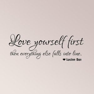 May include: A black wall decal featuring the cursive and print text: Love yourself first then everything else falls into line. A small black heart symbol precedes the name Lucille Ball, which is written in a bold, sans-serif font.