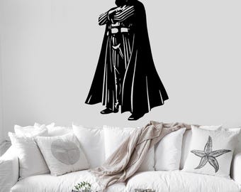 May include: A black wall decal featuring a stylized silhouette of a figure wearing a helmet, a long flowing cape, and a chest plate with vertical lines. The figure stands with arms crossed in a rigid posture, rendered in a high-contrast graphic style.