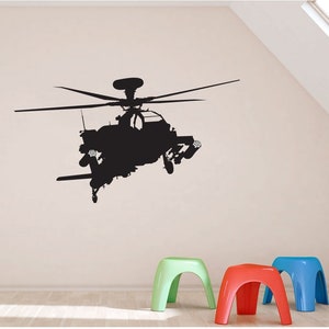May include: A black silhouette of a helicopter with detailed features, including rotors and weaponry, is displayed on a light-colored wall. Below, three colorful stools in green, red, and blue add a playful contrast to the scene.