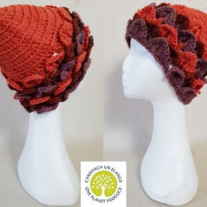 Puede incluir: Un gorro de crochet con un diseño texturizado en tonos marrones, naranjas y morados. El gorro se muestra en una cabeza de maniquí blanca.