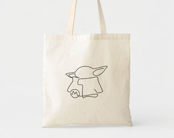 May include: A white canvas tote bag with a black line drawing of a character from the Star Wars series, The Mandalorian. The character is holding a small ball in its hand.