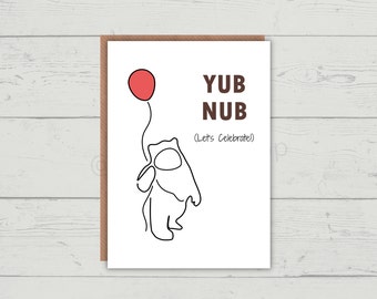 May include: A white card with a brown border and the text "YUB NUB (Let's Celebrate)" in brown text. A black line drawing of a bear holding a red balloon is on the card.