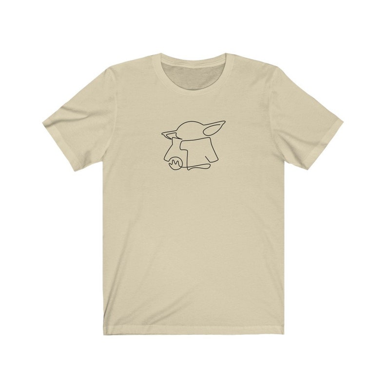 May include: A beige t-shirt with a black line drawing of a character from the Star Wars franchise, The Mandalorian, known as "The Child" or "Baby Yoda".