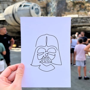 May include: A simple line drawing of Darth Vader's helmet on a white piece of paper.