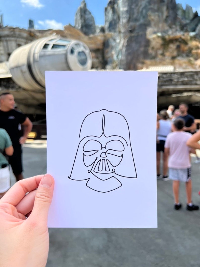 May include: A simple line drawing of Darth Vader's helmet on a white piece of paper.