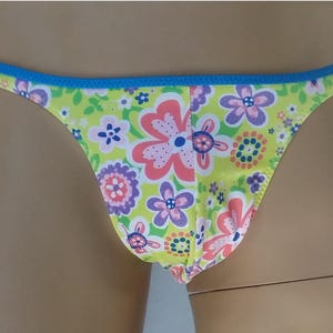 Puede incluir: Un par de ropa interior de estampado floral con ribete azul. La ropa interior tiene un fondo amarillo brillante con flores rosas, moradas y verdes.