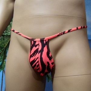 Puede incluir: Un tanga rosa y negro con estampado de tigre y tirantes finos. "EXAMPLE WITH LYCRA 27 TIGER and EDGE COLOR LYCRA A27" está escrito en la parte inferior de la imagen.