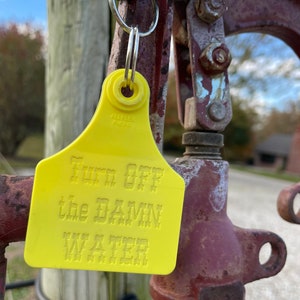 May include: Yellow plastic tag with the text "Turn off the DAMN WATER" attached to a rusty metal pipe with a black rubber band.