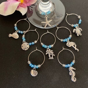May include: Set of eight blue and silver wine glass charms with various beach-themed charms, including a starfish, a turtle, a flamingo, a palm tree, a seashell, a sand dollar, a fish, and a seahorse.