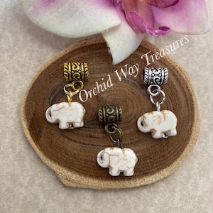 May include: Three white elephant charms with gold and silver bead caps. The charms are on a wooden surface with the text "Orchid Way Treasures" visible.