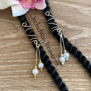 May include: Close-up of two pieces of black hair adorned with decorative hair jewelry. One piece features gold wire accents and white pearl beads, while the other has silver wire and white pearl beads. The text "Orchidway Treasures" is visible.