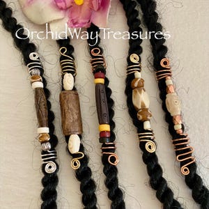 May include: Five sets of dreadlock beads with various wood and bone beads, copper and gold wire wraps, and silver beads. The beads are on black dreadlocks.