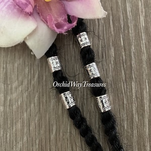 May include: Silver metal beads with a star pattern, used for hair extensions or braiding. The beads are on black hair strands.