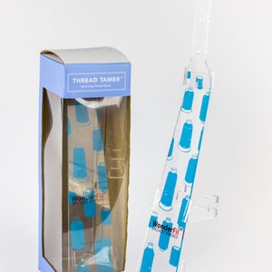 May include: A clear acrylic thread stand with a blue and white design, next to a blue and white box. The box and stand both feature the text "THREAD TAMER" and "WonderFil SPECIALTY THREADS". The stand is designed to hold spools of thread.