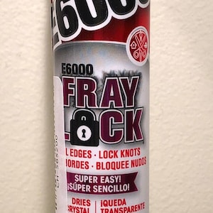 May include: A white tube of E6000 Fray Lock adhesive. The label includes the brand name, product name, and features like "dries clear" and "flexible." The tube contains 2 fl oz (59.1 mL) of adhesive.