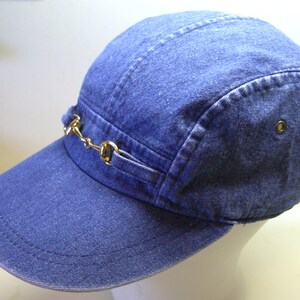 May include: A blue denim five-panel cap with a gold metal horse bit accent.