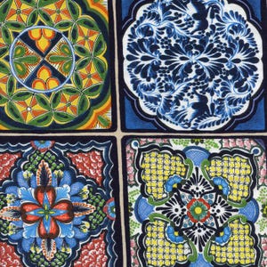 May include: Close-up of a fabric with four square panels, each featuring a unique, colorful, and intricate floral or geometric design. The panels showcase a variety of colors, including blue, yellow, red, green, and orange, with dark blue borders.