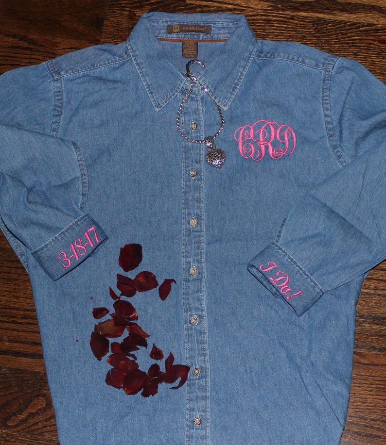 K&ouml;nnte beinhalten: Ein blaues Jeanshemd mit rosa Stickereien an den Manschetten und der Brust. Die Manschetten sagen "I Do!" und "3-18-17". Die Bruststickerei ist ein Monogramm mit den Buchstaben "C.R.O.".