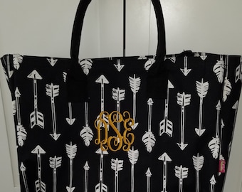 May include: Black tote bag with white arrow print and a gold monogram. The monogram is in the center of the bag.