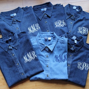 K&ouml;nnte beinhalten: Sieben Jeanshemden mit wei&szlig;en Stickereien. Jedes Hemd hat eine andere Monogramm-Stickerei auf der linken Brust.