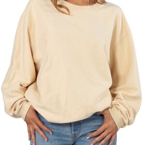 May include: A cream colored waffle knit sweater with long sleeves and a round neckline.