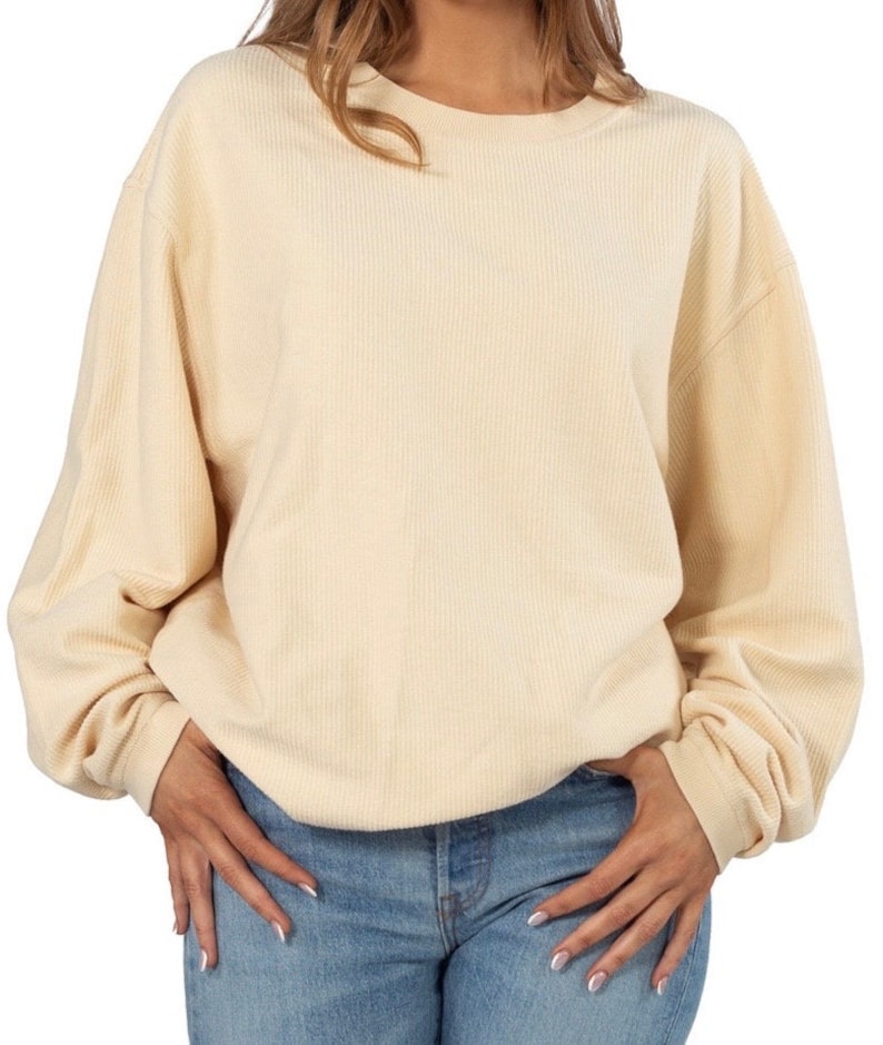 May include: A cream colored waffle knit sweater with long sleeves and a round neckline.