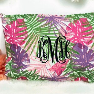 May include: A white canvas zippered pouch with a tropical leaf print in shades of pink, green, and purple. The pouch has a black drawstring and the monogram "KMH" is embroidered in black on the front.