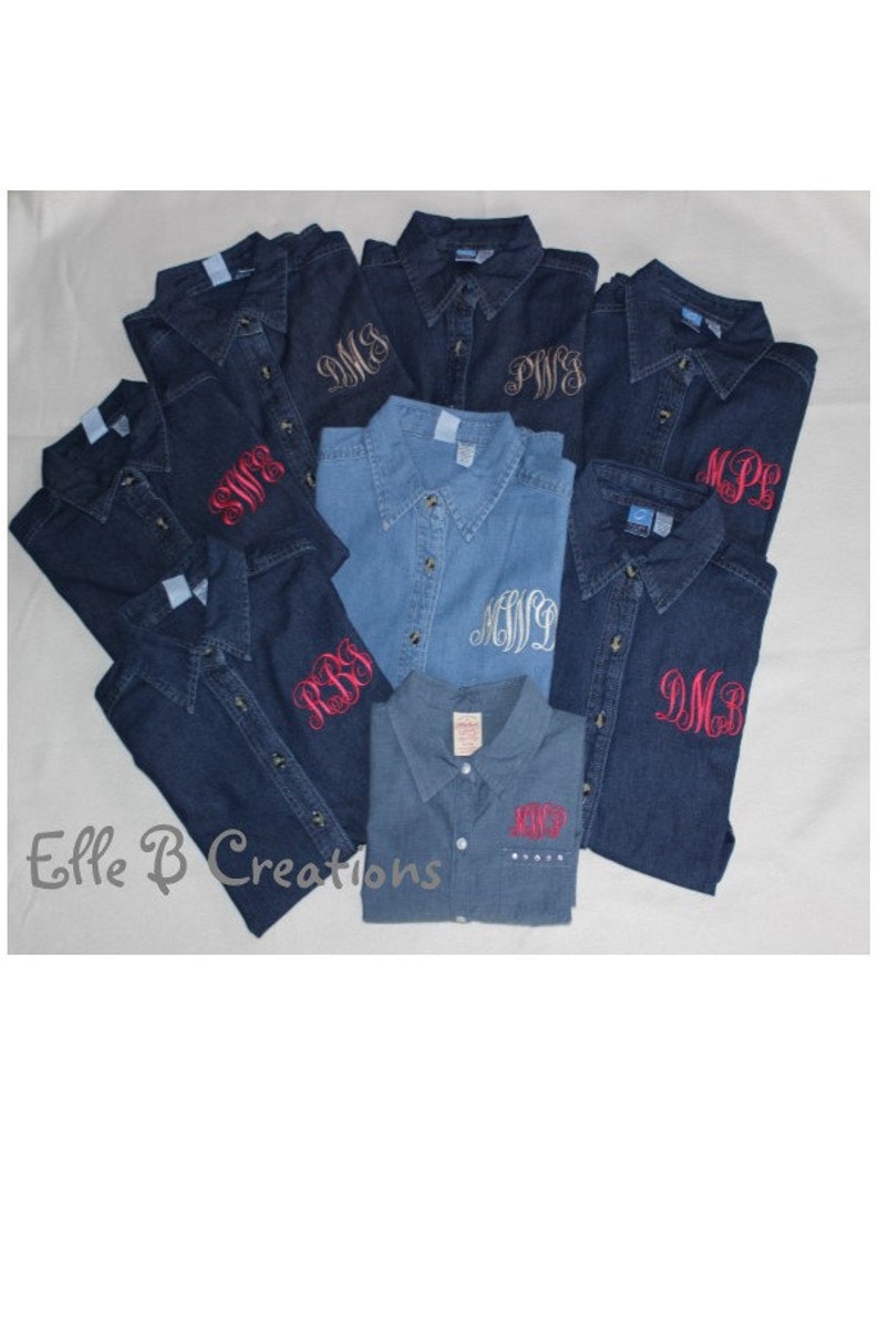 K&ouml;nnte beinhalten: Eine Gruppe von Jeanshemden mit verschiedenen gestickten Monogrammen in verschiedenen Farben. Die Hemden liegen auf einem wei&szlig;en Untergrund in einem Stapel. Der Text "Elle B Creations" ist am unteren Rand des Bildes sichtbar.