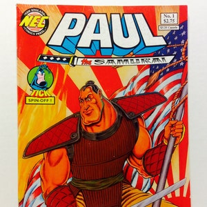 May include: Comic book cover featuring a muscular cartoon character in a red and brown samurai outfit holding a sword. The character is standing in front of an American flag and a Japanese flag. The title of the comic is "Paul the Samurai" and the issue number is "No. 1".