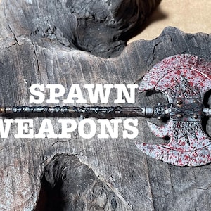 Puede incluir: Un hacha de doble hoja plateada y roja con un mango negro y plateado. El hacha está cubierta de pintura roja salpicada y tiene una punta afilada. El texto "SPAWN WEAPONS" es visible en la imagen.