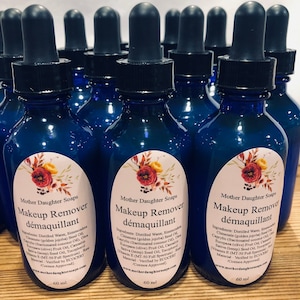 May include: A group of 10 blue glass bottles with dropper tops, each containing a makeup remover labelled "Makeup Remover d&eacute;maquillant" with a floral design and the ingredients listed. The bottles are 60 ml each.