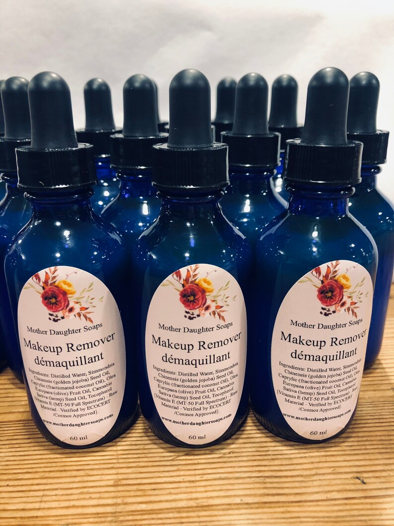 May include: A group of 10 blue glass bottles with dropper tops, each containing a makeup remover labelled "Makeup Remover d&eacute;maquillant" with a floral design and the ingredients listed. The bottles are 60 ml each.