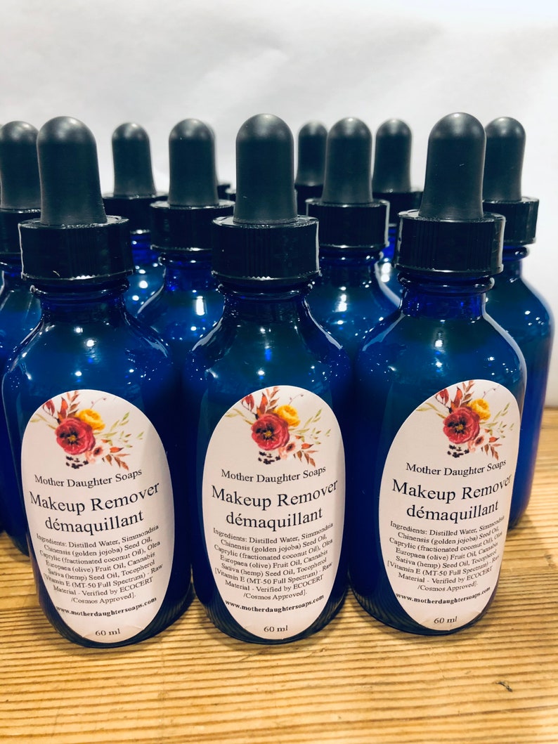May include: A group of 12 blue glass bottles with dropper tops, each containing 60 ml of makeup remover. The bottles have labels with the text "Mother Daughter Soaps" and "Makeup Remover d&eacute;maquillant" in white lettering. The labels also list the ingredients of the makeup remover.