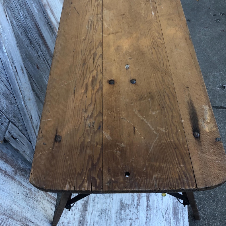 K&ouml;nnte beinhalten: Ein rustikaler Holztisch mit einer nat&uuml;rlichen Holzoptik. Der Tisch hat ein schlichtes Design mit einer rechteckigen Tischplatte und einem Metallgestell. Der Tisch ist aus massivem Holz gefertigt und hat eine Used-Look-Optik.